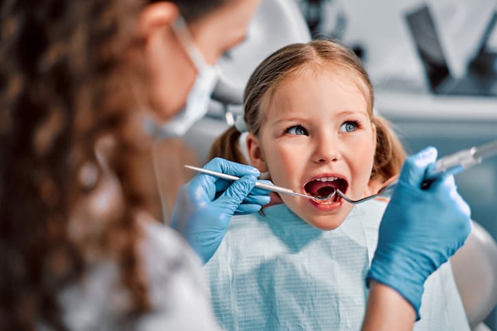 A young girl receives a gentle dental examination from a dentist during a routine checkup. The image represents children's dentistry, preventive dental care, early oral health assessments, and creating positive dental experiences for kids.